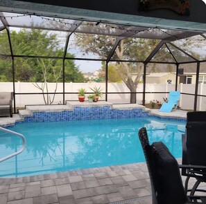A covered outdoor swimming pool with a tiled edge, a chair, and potted plants. - Beautiful home with heated saltwater pool in sought after Cape Coral, Florida. (Cape Coral)