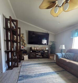 A living room with a television, wooden shelving, a sofa, and a patterned rug.