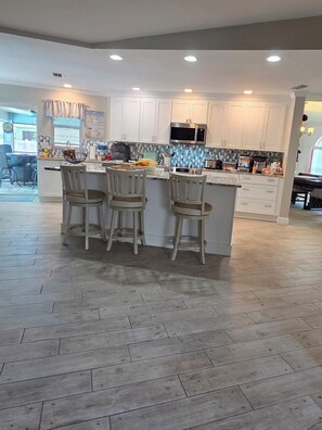 A modern kitchen with white cabinets, a central island with bar stools, and a microwave above the island.