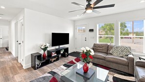A modern living room with a flat-screen TV, a ceiling fan, a leather sofa, and a glass coffee table. - NEW Modern Contemporary West Side Retreat (Colorado Springs)