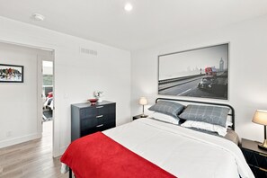 A bedroom with a bed, a dresser, a nightstand, a lamp, and a cityscape painting on the wall. - NEW Modern Contemporary West Side Retreat (Colorado Springs)