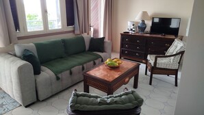 Un salon comprenant un canapé, une table basse avec des fruits, un meuble en bois, un téléviseur et un fauteuil.