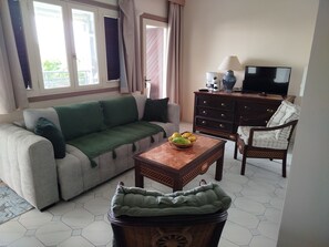 A living room with a sofa, a coffee table with fruits, a wooden cabinet, a television, and a chair. - Vrbo Property (st françois)