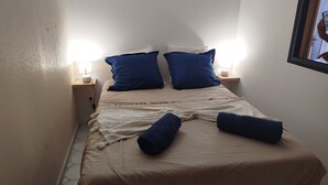 Un lit recouvert d’une couvre-lit beige et agrémenté de deux oreillers bleus, avec deux lampes de chevet placées de part et d’autre sur des tables de chevet en bois.
