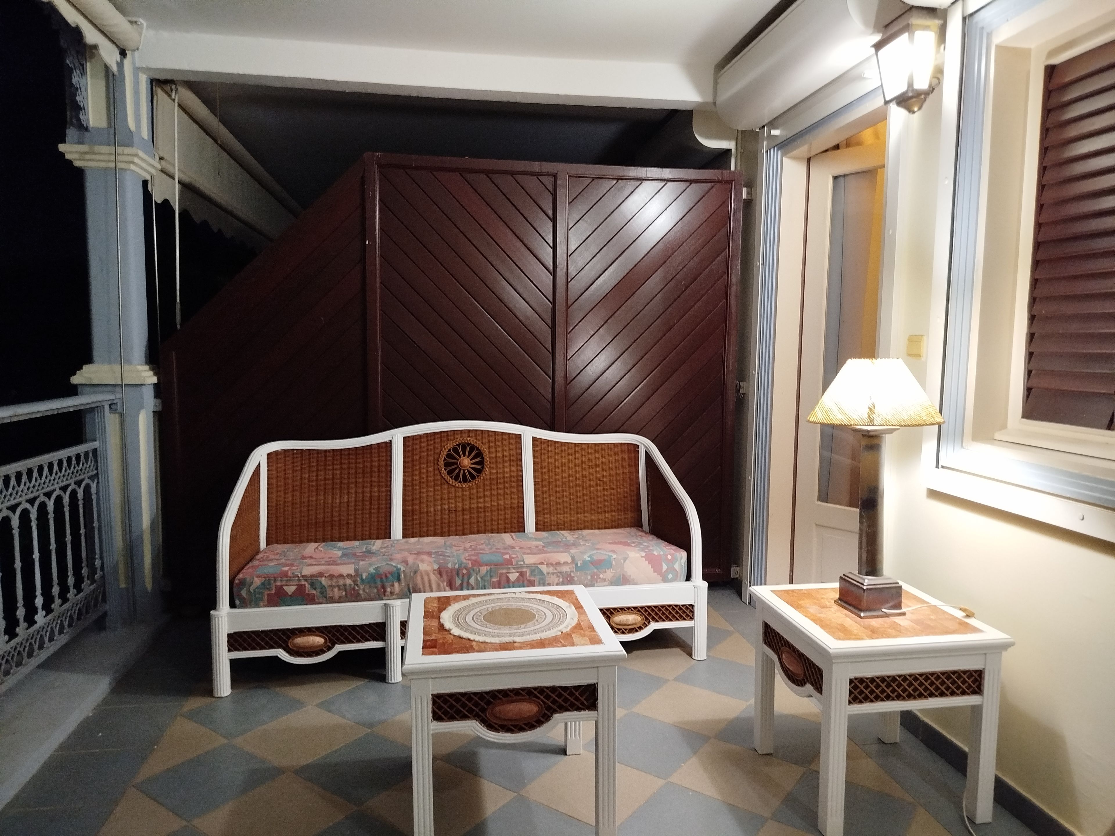 A room with a sofa, a small table, a lamp, and a window with blinds.