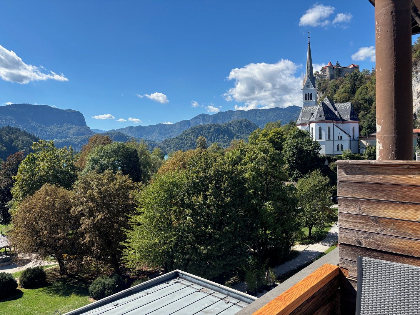 A view of a building with a prominent tower, surrounded by lush greenery and mountains in the background.
