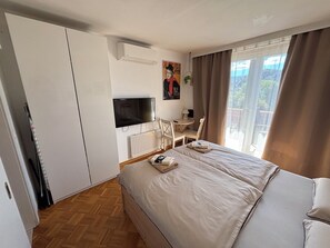 A hotel room with a bed, a desk, a chair, a television, and a window with curtains. - Bled Castle & Lake View Apartment (Bled)