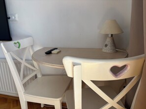 A small round table with a lamp, two white chairs with heart designs, and a remote control on the table. - Bled Castle & Lake View Apartment (Bled)
