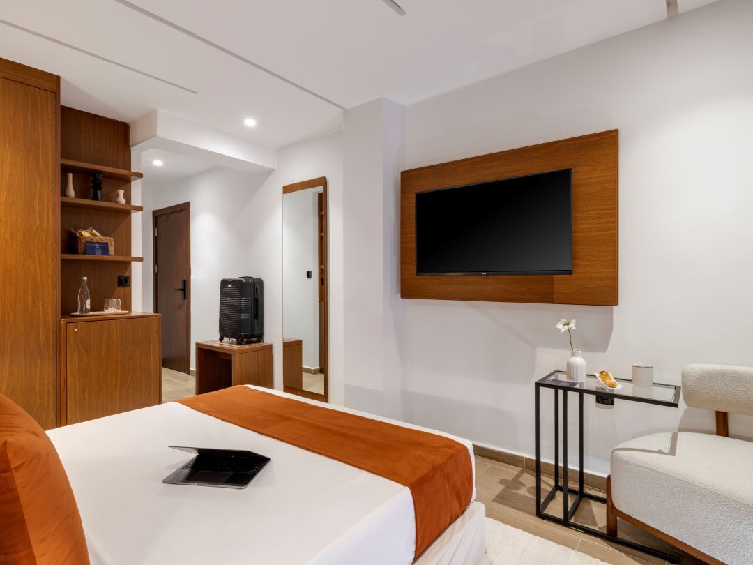 Une chambre d’hôtel moderne équipée d’un lit, d’un téléviseur fixé au mur, d’un bureau avec un ordinateur et d’une chaise.