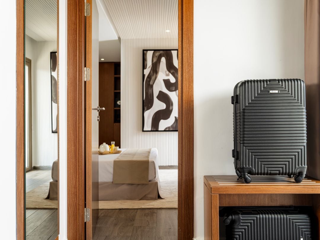 Una habitación de hotel con una cama, una mesita de noche, una obra de arte colgada en la pared y una maleta sobre un atril de madera.