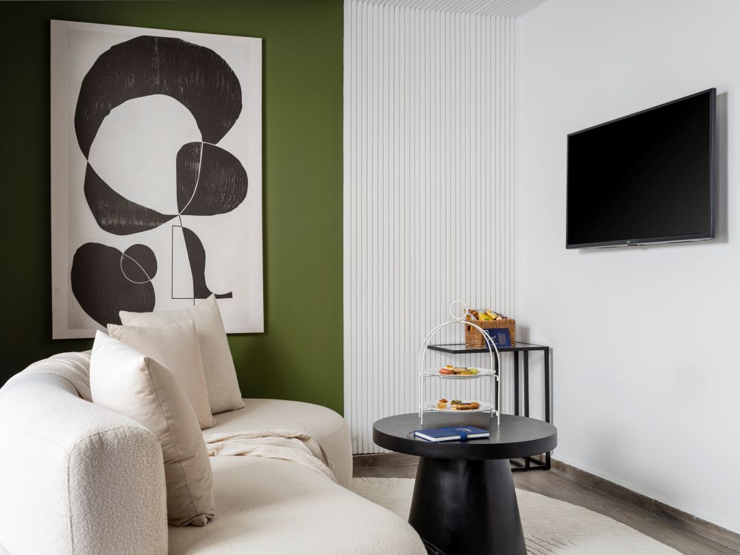 Un salon moderne avec un canapé d’angle, une table basse noire, un téléviseur fixé au mur et un objet décoratif.