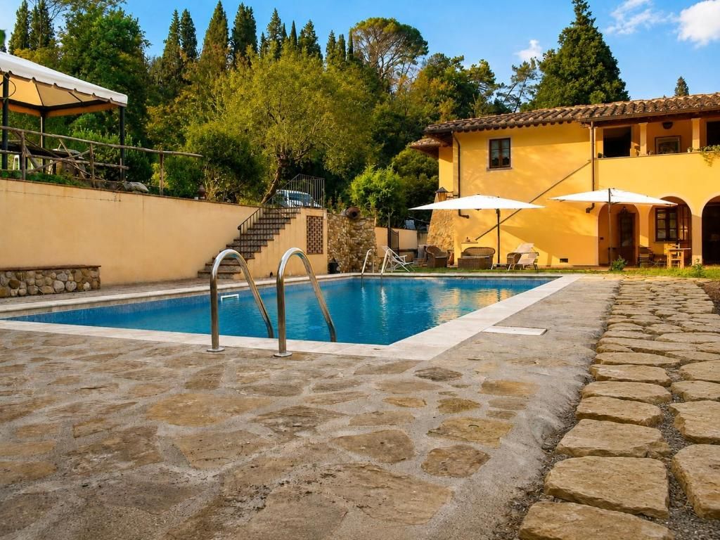 A swimming pool with a stone deck, a covered seating area, and a building with a yellow facade.