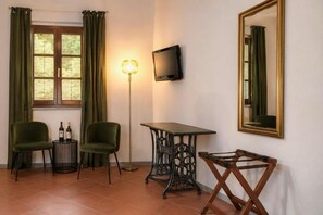 A room with two green chairs, a small round table with bottles, a floor lamp, a television on the wall, and a large mirror. - Hotel Sor Paolo (San Casciano in Val di Pesa)