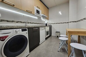 A compact kitchen with a washing machine, microwave, and a small dining area with stools.