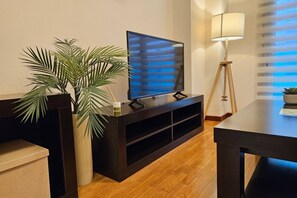 Una sala de estar moderna con una televisión de pantalla plana sobre un mueble de madera oscura, una lámpara de pie y una planta grande en maceta.