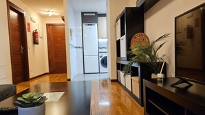 Een moderne woonkamer met een houten vloer, een flatscreen televisie, een potplant en een gang die leidt naar een keukenhoek.