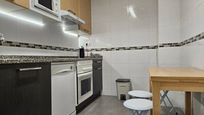 Een compacte keuken met een vaatwasser, oven, magnetron en een klein tafeltje met krukjes.