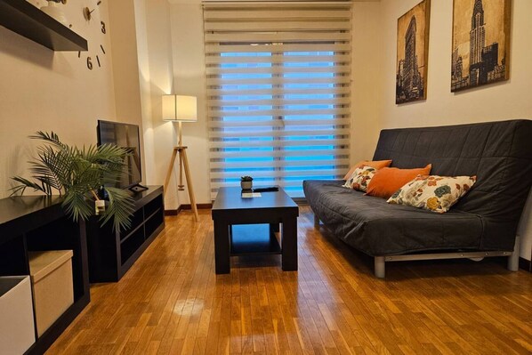 A living room with a dark sofa, a small table, a lamp, and a plant.
