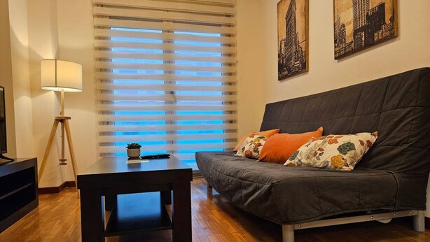 Een woonkamer met een bank, een salontafel, een vloerlamp en een raam met jaloezieën.