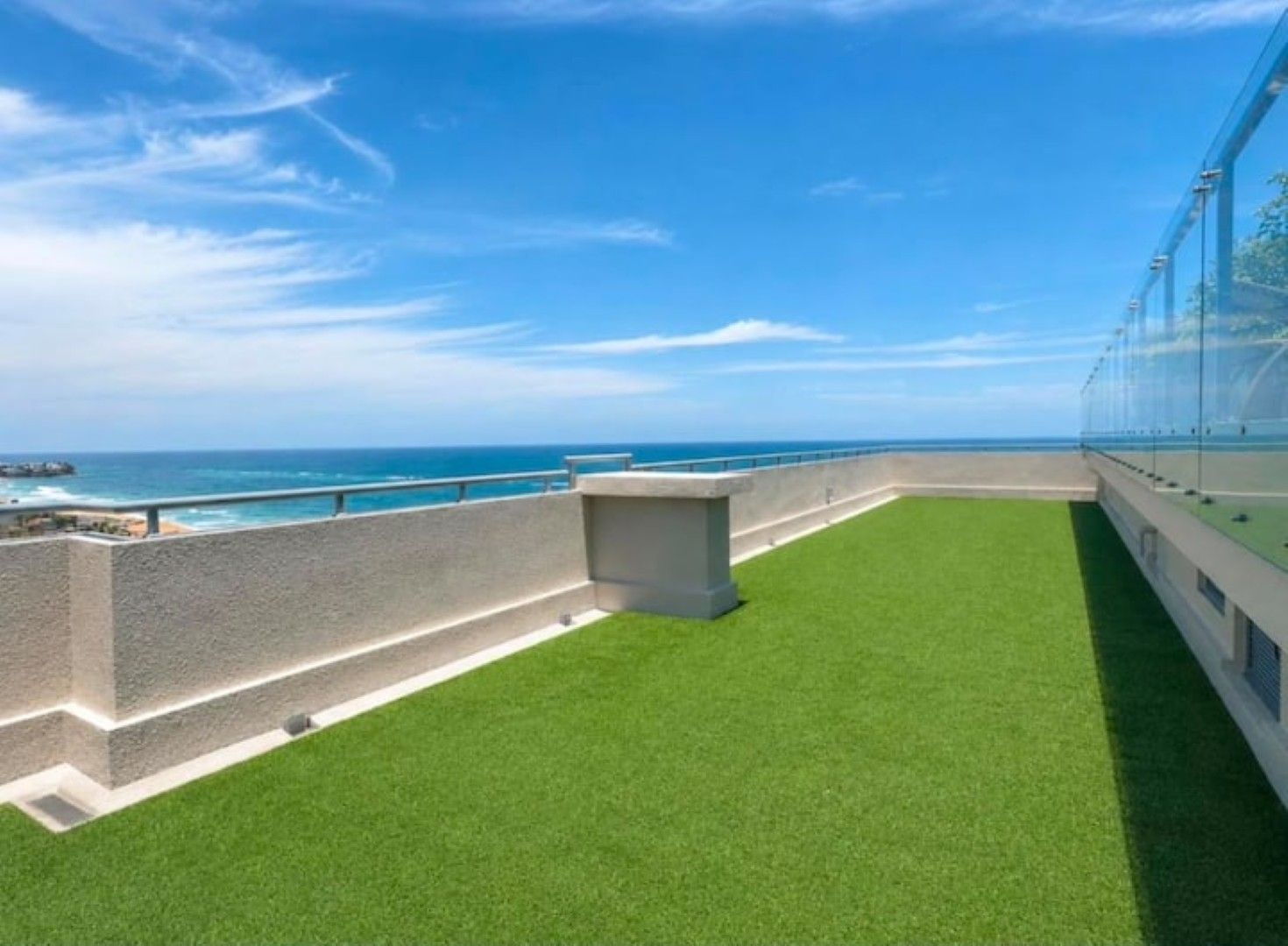 A rooftop terrace with a view of the ocean, a glass enclosure, and a concrete wall.