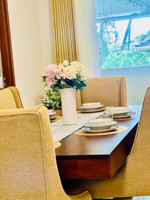 A dining table set with plates, a vase of flowers, and a window with a view of greenery. - Premium Luxury Apartment.Prime location (Dehiwala-Mount Lavinia)