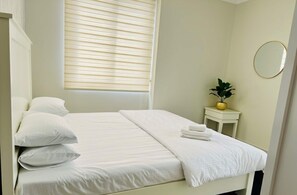 Ein ordentlich bezogenes Bett mit Kissen und einem gefalteten Handtuch, eine Zimmerpflanze und ein runder Spiegel auf einem kleinen Tisch.