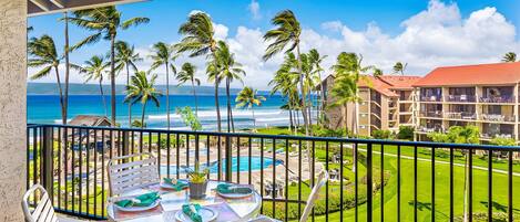 A balcony with a table set for dining, overlooking a pool and a beachfront hotel.