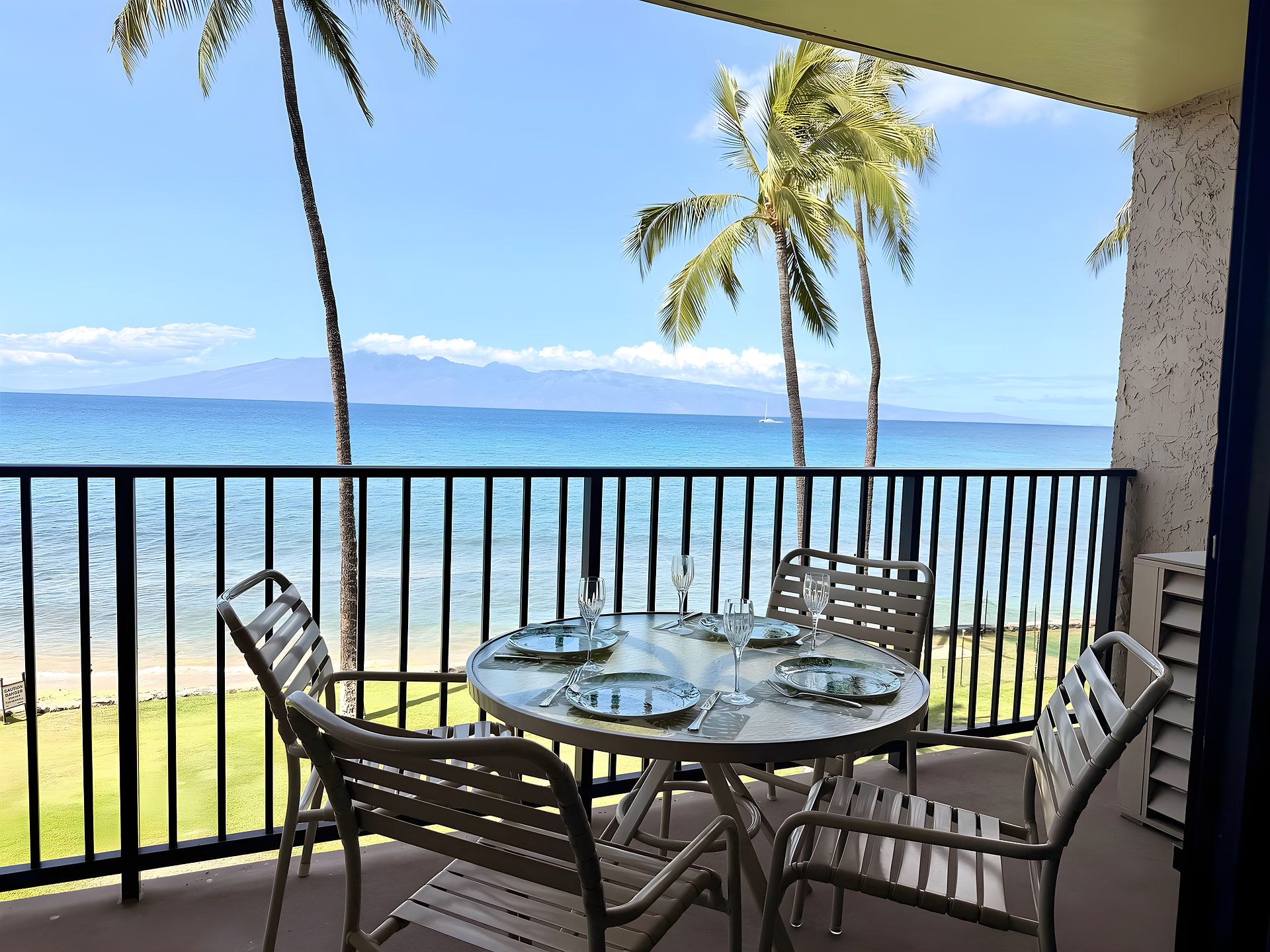 Un balcón con una mesa lista para comer, con vistas a una playa con palmeras y el océano.