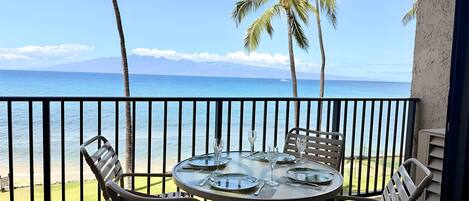 Un balcón con una mesa lista para comer, con vistas a una playa con palmeras y el océano.