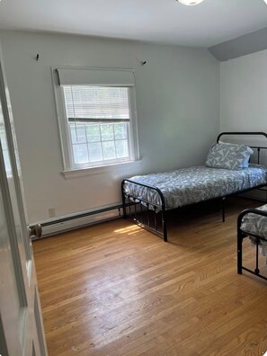 Ein kleines Zimmer mit einem Einzelbett, Fenster, Holzboden und Heizkörper.