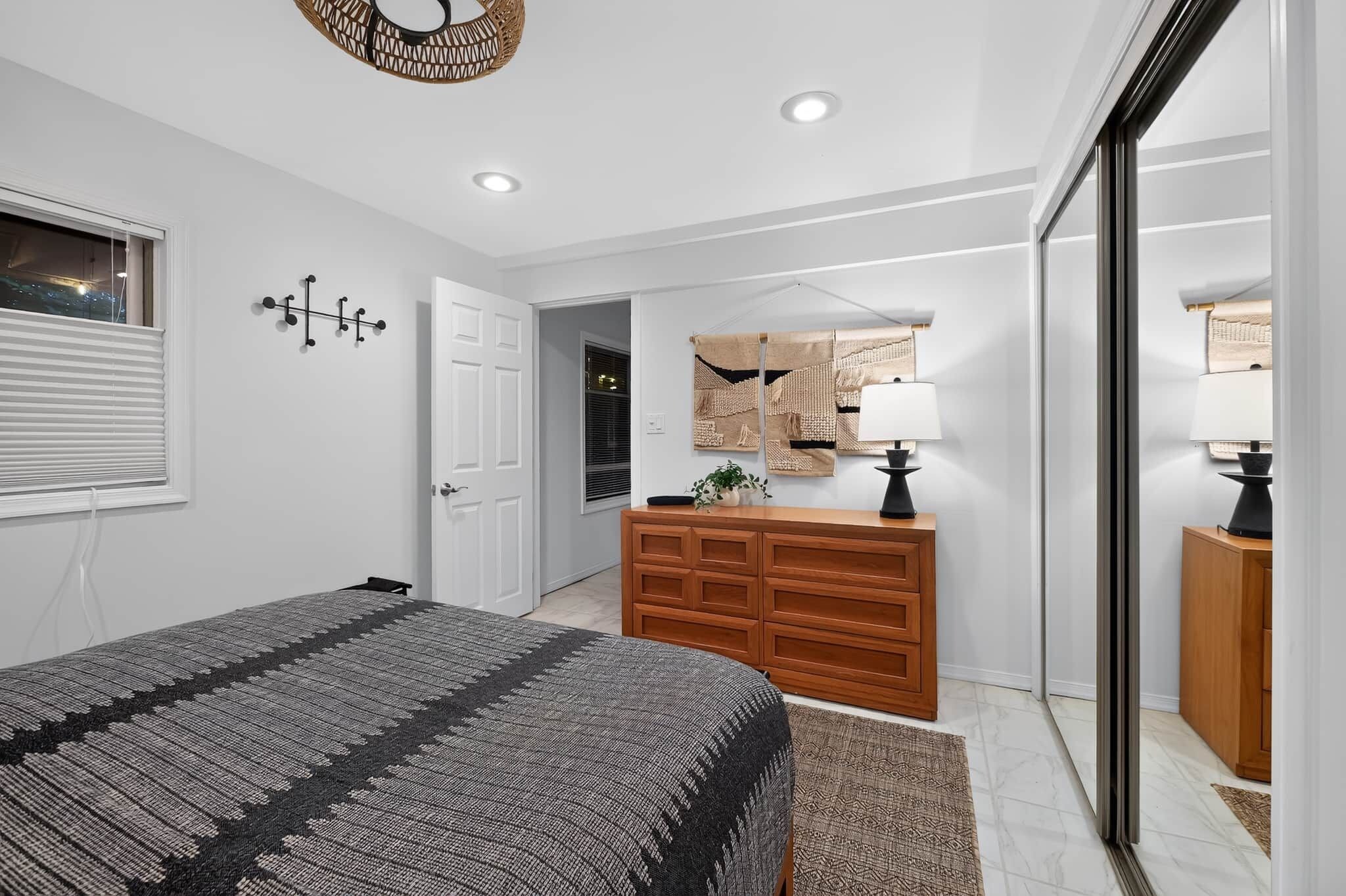 A bedroom with a bed, dresser, mirror, and a window with blinds.