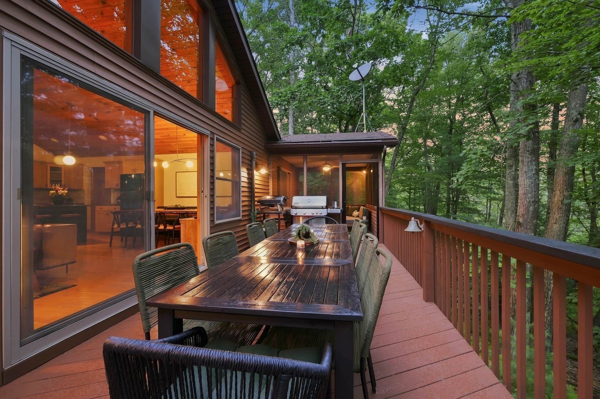 An outdoor deck with a dining table and chairs, surrounded by glass walls and a wooden deck railing.