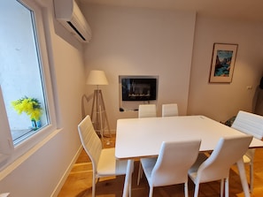 A modern dining area with a white table and chairs, a standing lamp, a flat-screen TV, and a framed picture on the wall. - Renovated 3-Bedroom Apartment, 70 m²: Heart of the Old Port - Calanque Beach (La Ciotat)