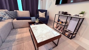Una sala de estar con sofá, sillón, mesa de centro y estantería.