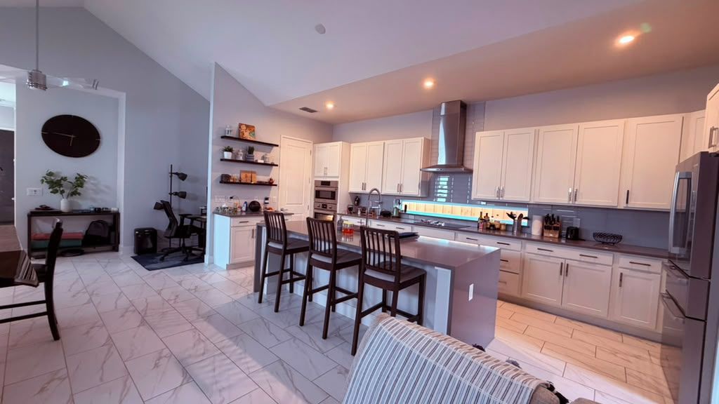 A modern kitchen with white cabinetry, a central island with bar stools, and a built-in oven.