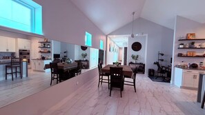 Una cocina moderna con armarios blancos, un comedor con mesa y sillas, y un espejo grande que refleja el espacio.
