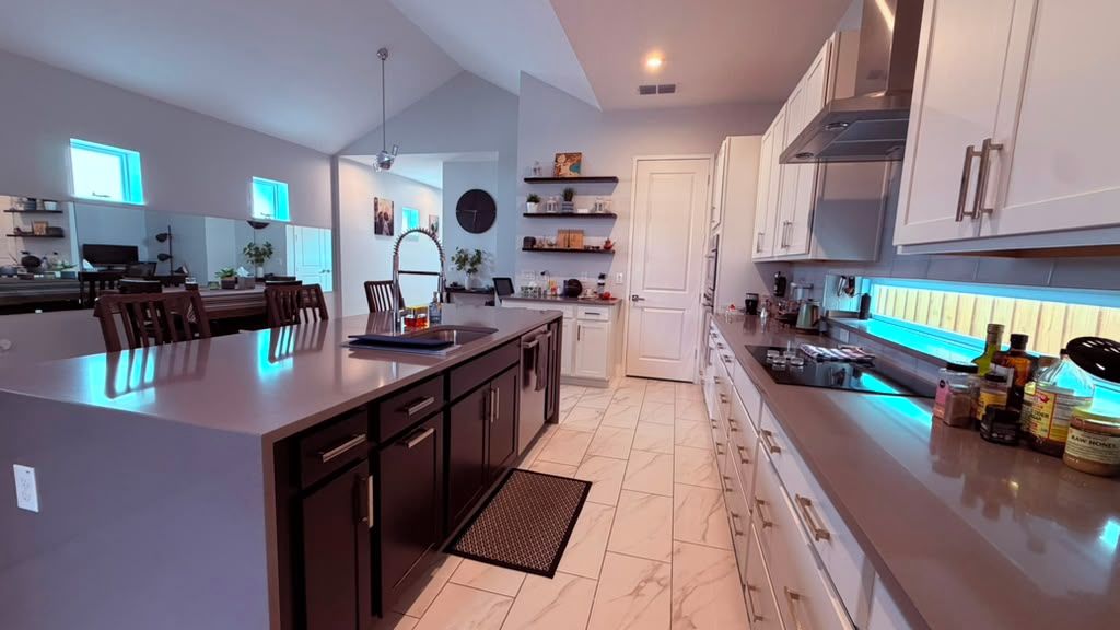 A modern kitchen with white cabinets, a central island, and a dining area with chairs.
