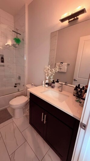 Un baño con cabina de ducha de vidrio, inodoro blanco, tocador con espejo y lavamanos.