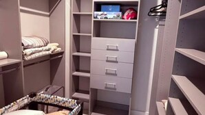 A walk-in closet with multiple shelves, drawers, and a bed with a patterned bedspread. - Modern 3BR Haus in Lake Nona Medical City (Orlando, FL, 32827)