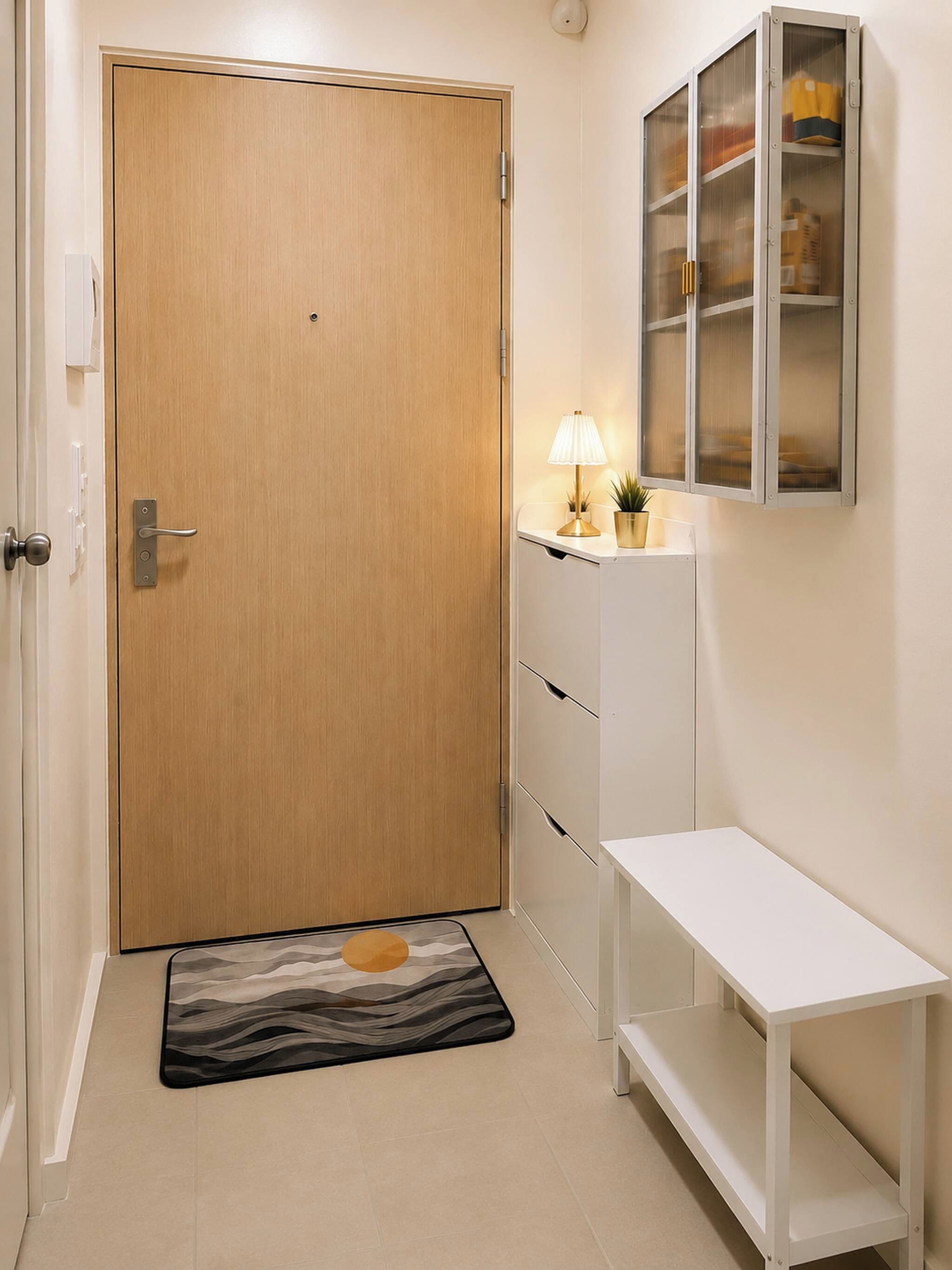 Un couloir avec une porte en bois, un banc blanc, une petite table avec une lampe et un meuble avec des portes en verre.