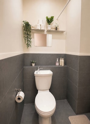 A modern bathroom with a toilet, a sink, and a mirror. There are toiletries on a shelf and a plant hanging on the wall. - The Sky Nook Cubao Near Gateway & MRT (Quezon City)