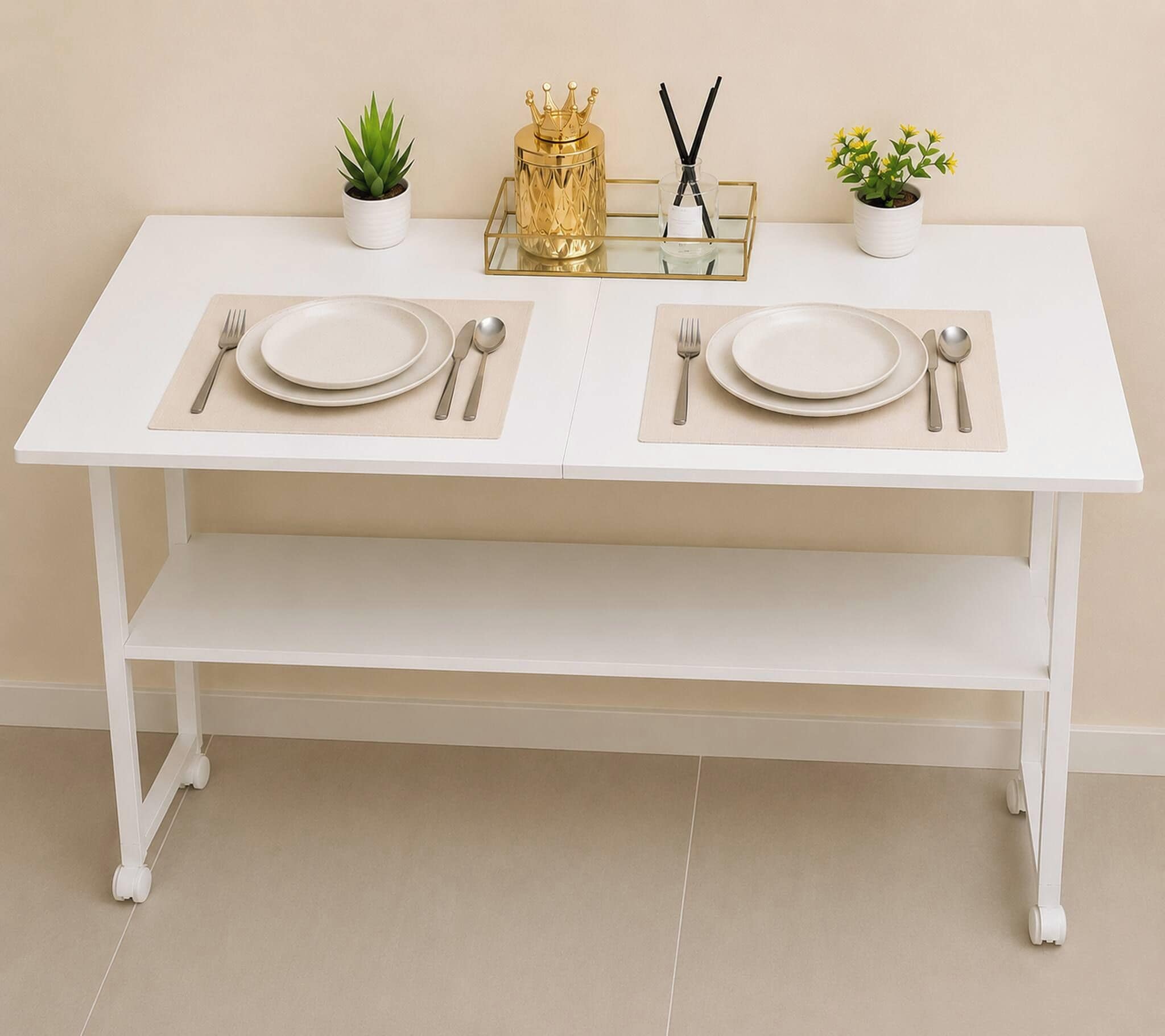 Mesa de jantar branca com dois jogos de pratos, talheres e guardanapos, adornada por pequenas plantas em vasos e um objeto dourado decorativo.