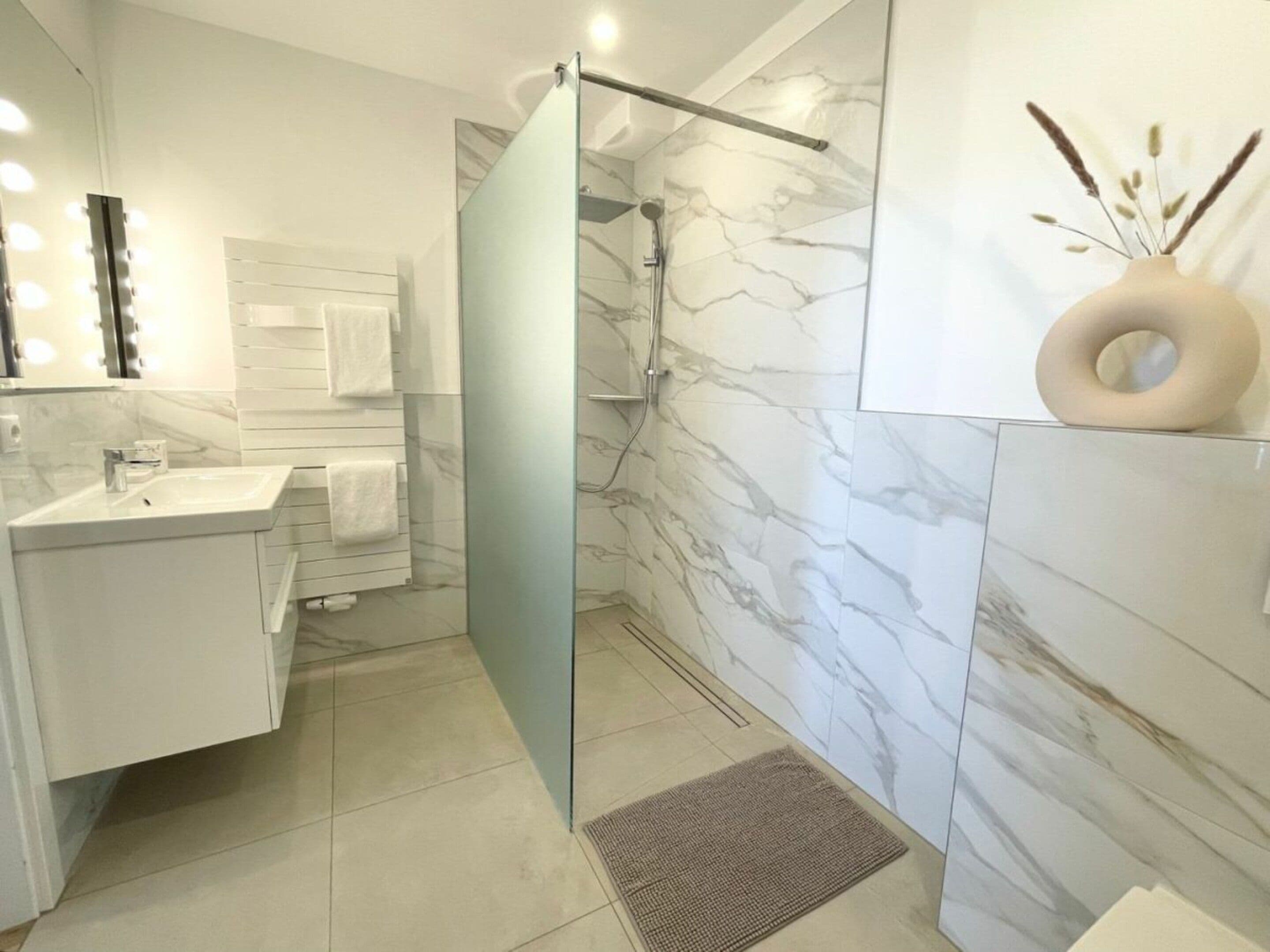 Une salle de bain moderne avec une douche à parois de verre, un lavabo blanc et des murs en marbre.