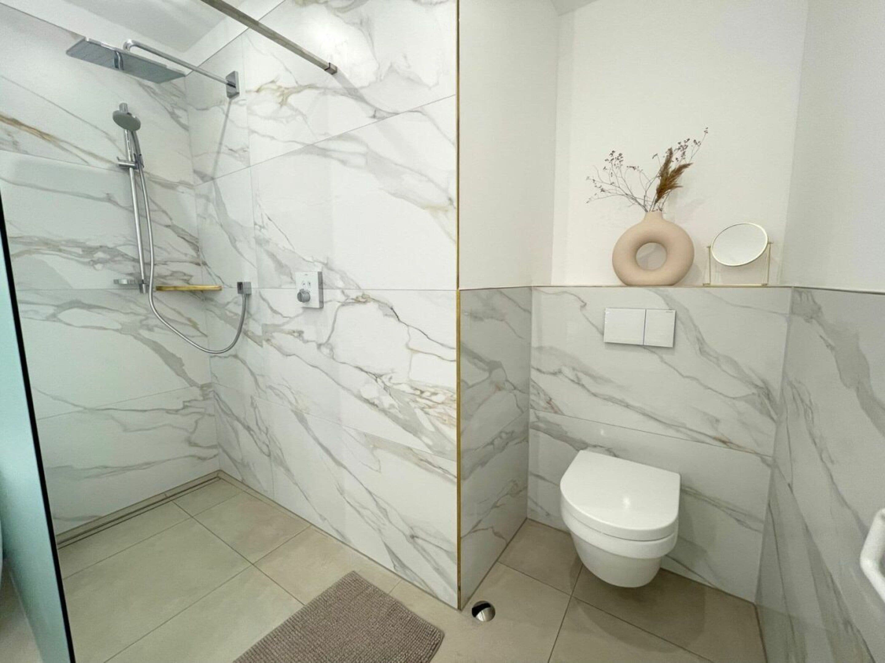 Un baño con ducha, inodoro y un pequeño florero decorativo.