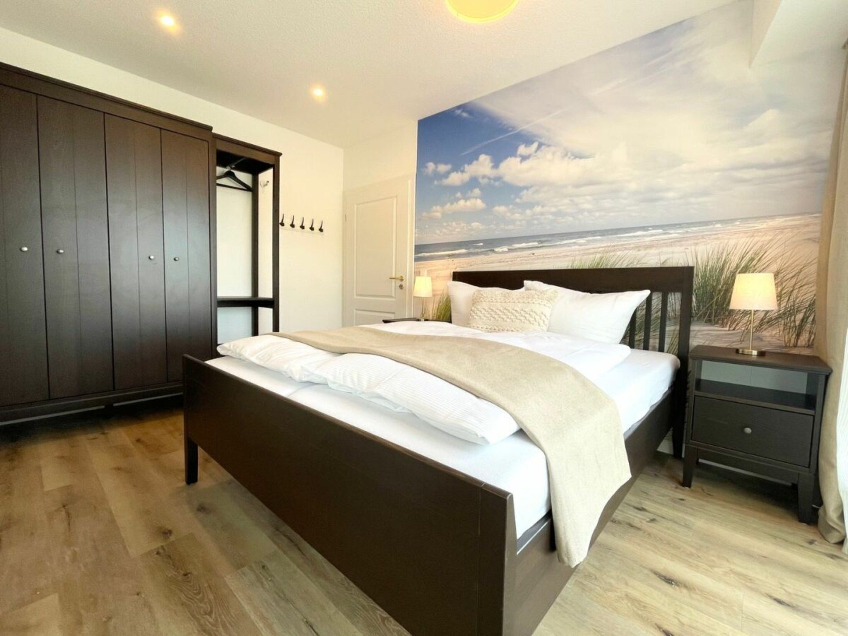 Une chambre à coucher comprenant un lit, une table de chevet, une armoire et une fresque murale sur le thème de la plage.