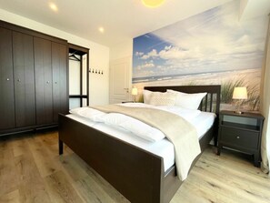 Une chambre à coucher comprenant un lit, une table de chevet, une armoire et une fresque murale sur le thème de la plage.