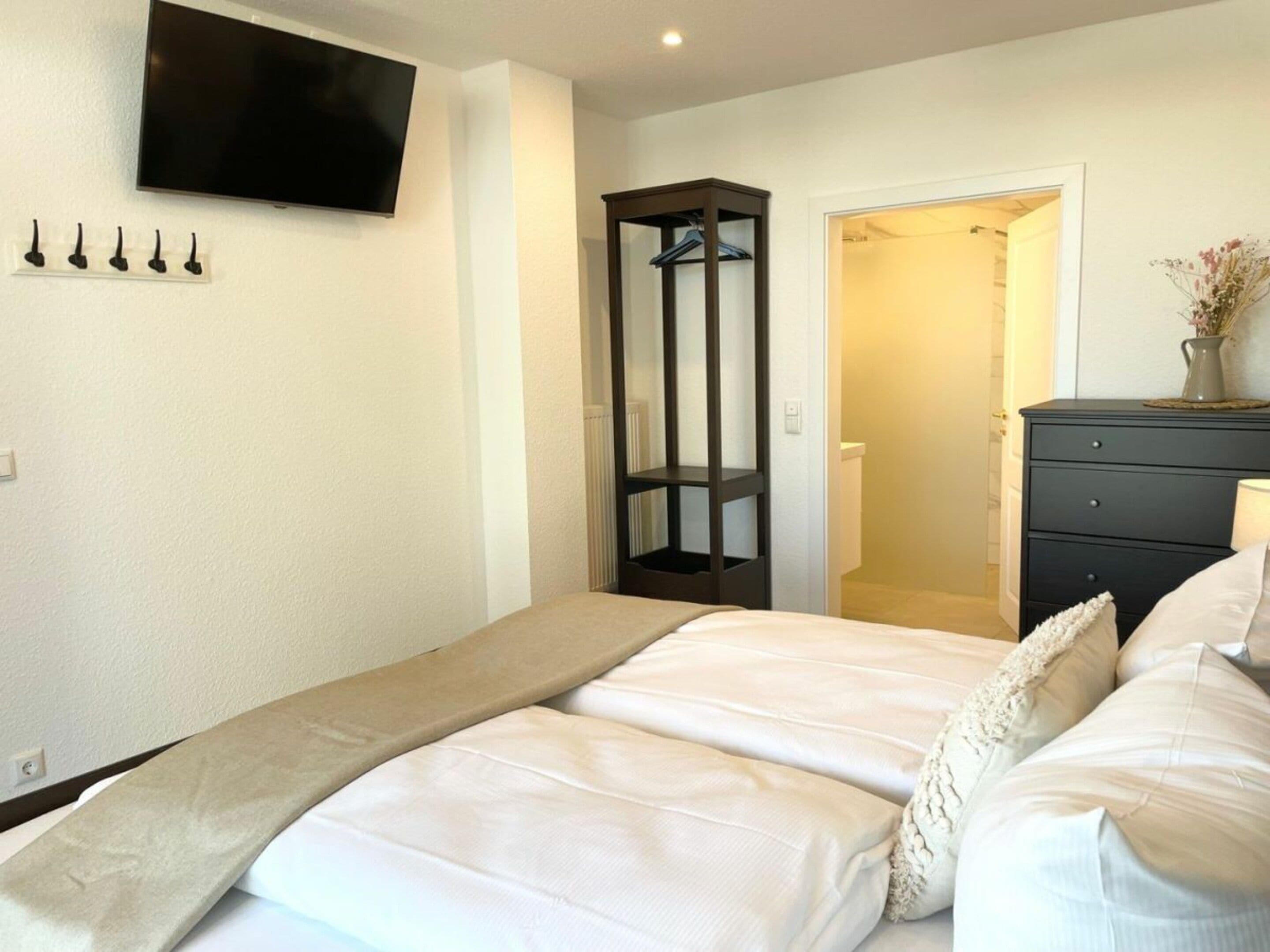 Un dormitorio con cama, televisor en la pared, armario y cómoda.
