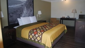 A hotel room with a bed, a desk, a chair, a television, and a large picture on the wall. - Heritage Inn and Suits (San Bernardino)