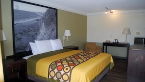 A hotel room with a bed, a desk, a chair, a television, and a large painting on the wall. - Heritage Inn and Suits (San Bernardino)
