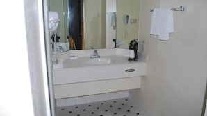 A bathroom with a white sink, a mirror, a hairdryer, and a towel rack. - Heritage Inn and Suits (San Bernardino)